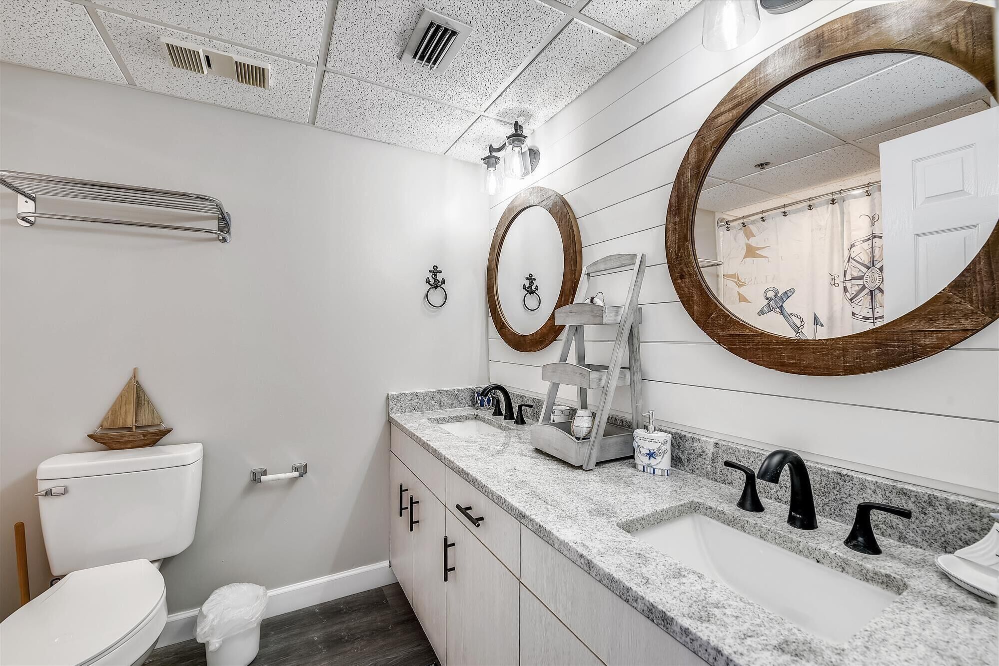 A modern bathroom with a white toilet, a sink with a marble countertop, and two large mirrors with wooden frames.