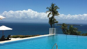 A pool with a view of the ocean, a palm tree, and lounge chairs. - Romance Nest in Samana 7-202 (Samaná)