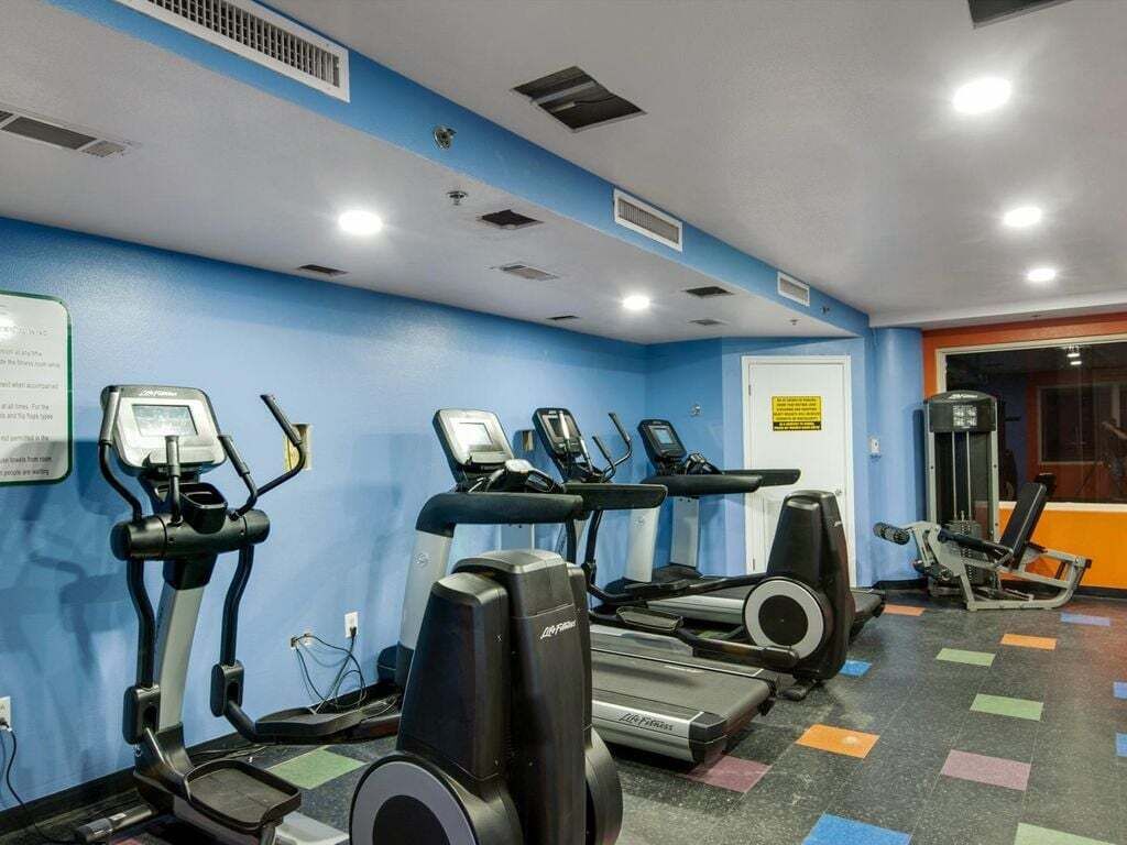 Ein Fitnessraum mit Laufbändern und Ellipsentrainern, einer blauen Wand und einem farbenfrohen Boden.