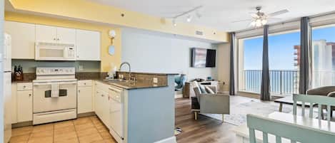 A modern kitchen with a microwave, oven, and sink, a dining area with a table and chairs, and a balcony with a view.