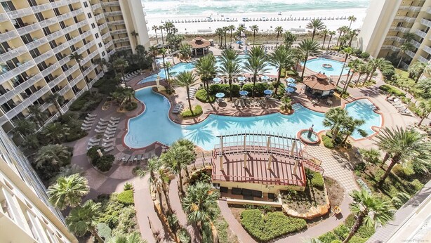 A resort with multiple swimming pools, palm trees, and a beach view.