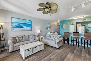 A living room with two sofas, a coffee table, a dining area with a table and chairs, and a ceiling fan.