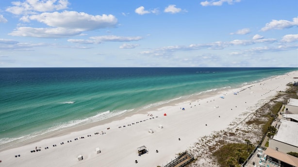 A beach with a long stretch of sand, a few beach umbrellas, and a few beach huts.