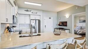 A modern kitchen with white cabinets, a stainless steel refrigerator, and a large island with a sink.