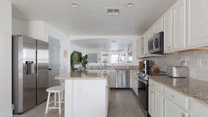 A modern kitchen with white cabinetry, stainless steel appliances, a granite countertop, and a central island with stools.