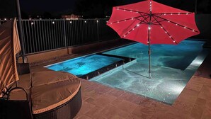 A swimming pool with a red umbrella, a chair, and a fence.