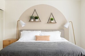 A neatly arranged bedroom with a bed, bedside lamps, a nightstand, and two wall-mounted shelves with plants. - Copper Cactus House: Pool, Spa, Golf! (Queen Creek)