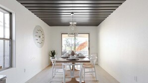 A modern dining area with a wooden table, white chairs, a chandelier, and a view through a glass door.