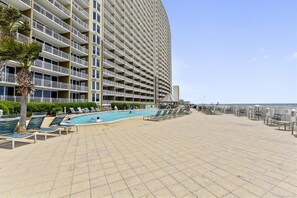 A high-rise hotel with a swimming pool, sun loungers, and a beach view.