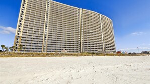 Un grand hôtel à plusieurs étages, à la façade uniforme, situé juste à côté d’une plage de sable.