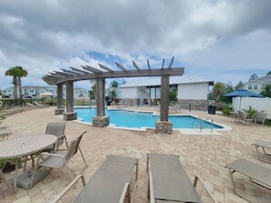 Un espace piscine aménagé avec des chaises longues, une pergola et une terrasse dallée de pierres.