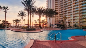 A hotel pool area with palm trees, lounge chairs, and a high-rise building in the background.