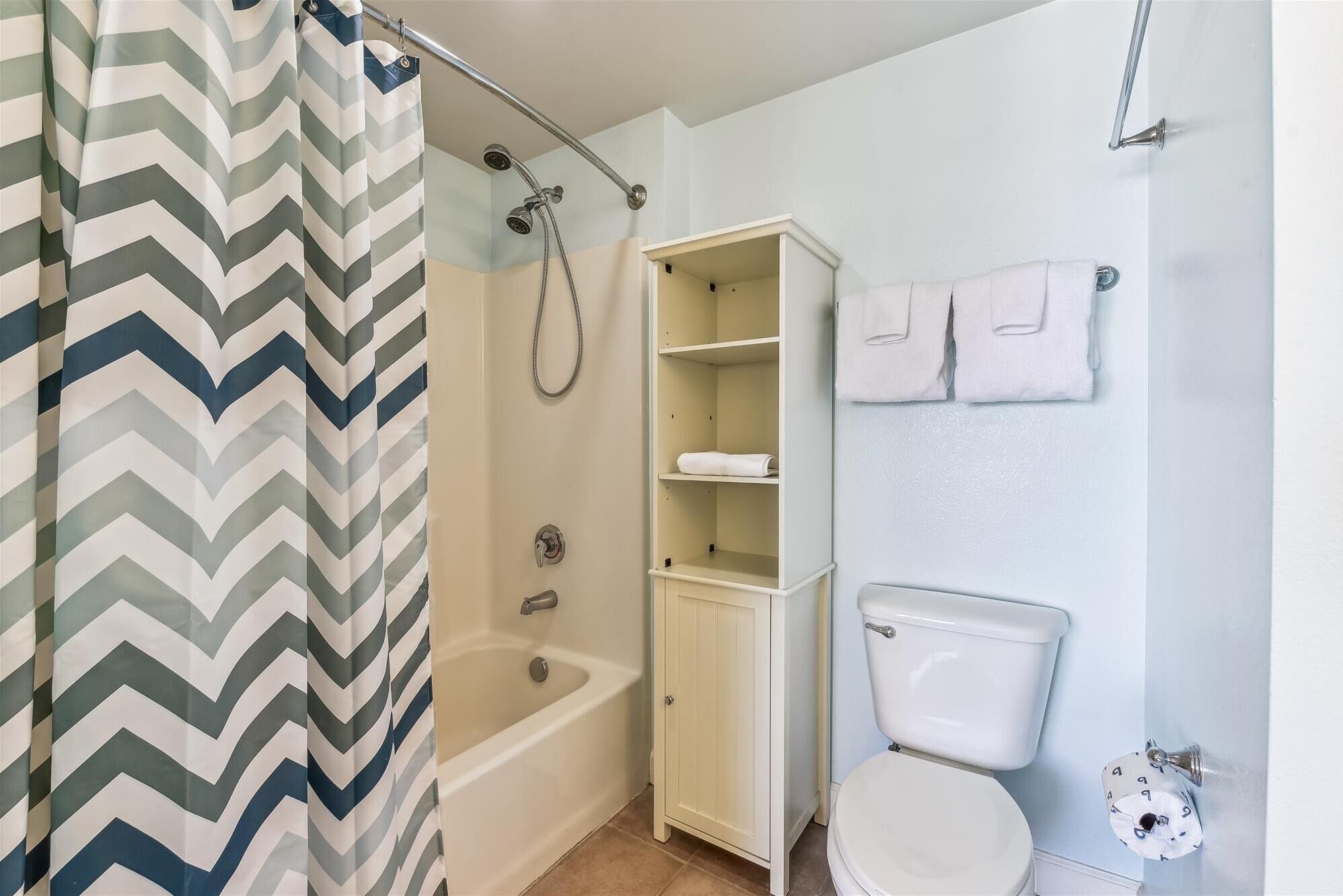 A bathroom with a shower, a bathtub, a toilet, and a storage cabinet.