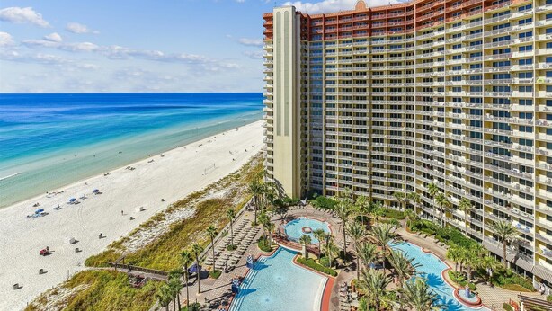Een hoog hotel met uitzicht op het strand, een zwembad en een strand met parasols.