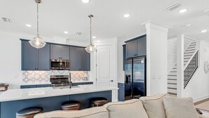 A modern kitchen with a central island, bar stools, and pendant lighting.