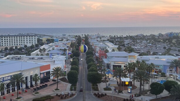 Un paisaje urbano costero con una calle principal que lleva a la playa, con edificios comerciales, un hotel grande y una estructura esférica de colores distintivos.