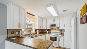 Una cocina moderna con armarios blancos, encimera de granito, microondas integrado, horno y refrigerador.