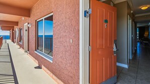 A hotel corridor with a red door, a window with a view of the sea, and a number sign above the door.