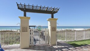 A beach entrance with a pergola, white columns, and a metal gate.