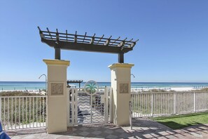 Una entrada a la playa con una pérgola, columnas blancas y una reja de metal.