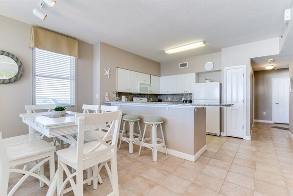 A modern kitchen with white cabinetry, a central island with stools, a microwave, and a refrigerator.