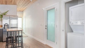 A modern kitchen with a wooden ceiling, a built-in refrigerator, a dining table with two stools, and a washing machine. - Kordeluxe Row #3 Studio Townhouse (Cedar City)