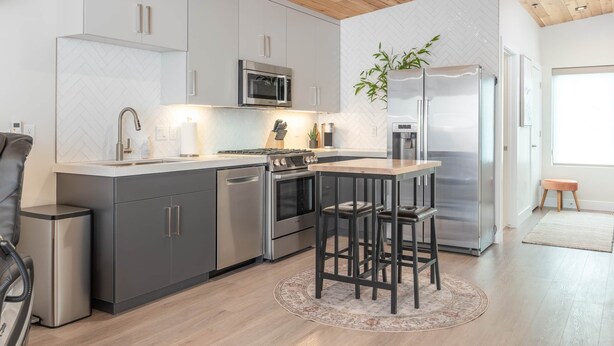 A modern kitchen with grey cabinets, stainless steel appliances, a wooden ceiling, and a round rug. - Kordeluxe Row #3 Studio Townhouse (Cedar City)