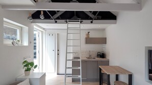A modern kitchen with a wooden table and stools, a white ladder, and a view of the adjacent living area. - The Roost - Cottage (Zandvoort)