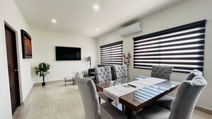 A modern dining area with a rectangular table, grey upholstered chairs, and a flat-screen TV mounted on the wall. - Aleman Apartments  (Mazatlán)