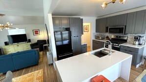 A modern kitchen with grey cabinets, a black refrigerator, and a microwave. There is a dining area with a blue sofa and orange stools. - Pet friendly, 3 bed/2ba home minutes from downtown/Ivy House/beach/bike trail. (Saugatuck)