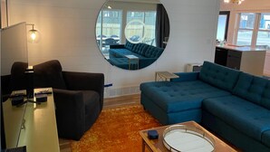 A modern living room with a large round mirror, a blue sofa, a small table, and a ceiling fan. - Pet friendly, 3 bed/2ba home minutes from downtown/Ivy House/beach/bike trail. (Saugatuck)