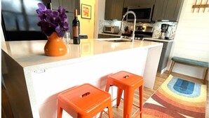 A modern kitchen with a white countertop, two orange stools, a colorful rug, and a bottle of wine on the counter. - Pet friendly, 3 bed/2ba home minutes from downtown/Ivy House/beach/bike trail. (Saugatuck)