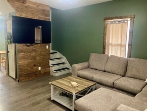 A living room with a sofa, a coffee table, a staircase, and a window with curtains.