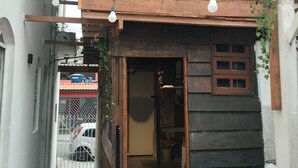 A narrow alleyway with a wooden building, a metal gate, and a tiled floor. - Guarulhos budget hostel with shared space: bedroom-bathroom-kitchen-living room (Jardim Cristina Guarulhos)