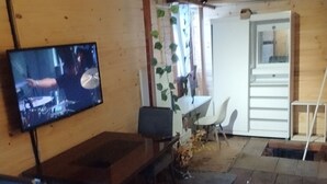 A room with a television mounted on the wall, a wooden ceiling, a dining table with chairs, and a hanging plant. - Guarulhos budget hostel with shared space: bedroom-bathroom-kitchen-living room (Jardim Cristina Guarulhos)