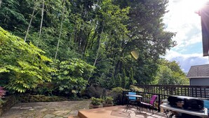 A wooden deck with stone flooring, surrounded by lush greenery and a wooden fence.