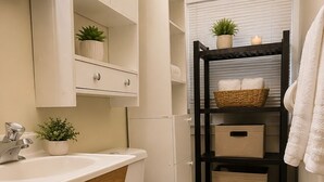 A compact bathroom with a toilet, sink, wooden cabinet, and a shelf with plants. - Charming 2-bedroom apartment in delightful Dearborn - no kitchen and no shower (Dearborn)