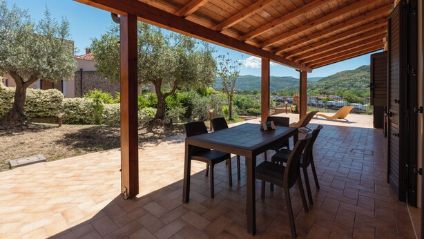An outdoor patio with a wooden pergola, a table with chairs, and a view of the surrounding landscape including trees and hills. - Apartment with large outdoor space available (Agropoli)
