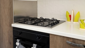 A kitchen with a gas stove, a white countertop, and wooden cabinets. - Apartment with large outdoor space available (Agropoli)