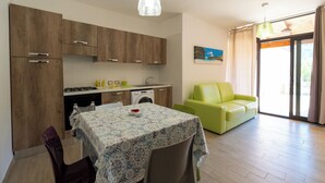 A modern kitchen with wooden cabinets, a dining table with a lace tablecloth, and a green sofa in a bright living area with a large window. - Apartment with large outdoor space available (Agropoli)