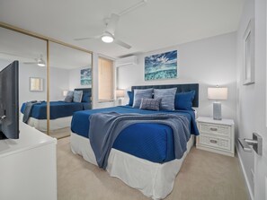 Une chambre à coucher avec un grand lit, un ventilateur de plafond, une table de chevet, un miroir et un tableau accroché au mur.
