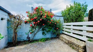 A stone-paved courtyard with a white wooden fence and a flowering plant climbing a wall.