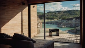 Une chambre dotée d’une grande fenêtre donnant sur un paysage magnifique, avec une rivière et des collines en toile de fond.