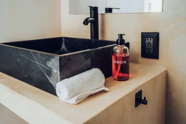 A bathroom with a black marble sink, a white towel, and a bottle of JABON soap. - Wander Cabins Dehe (Cadereyta de Montes)