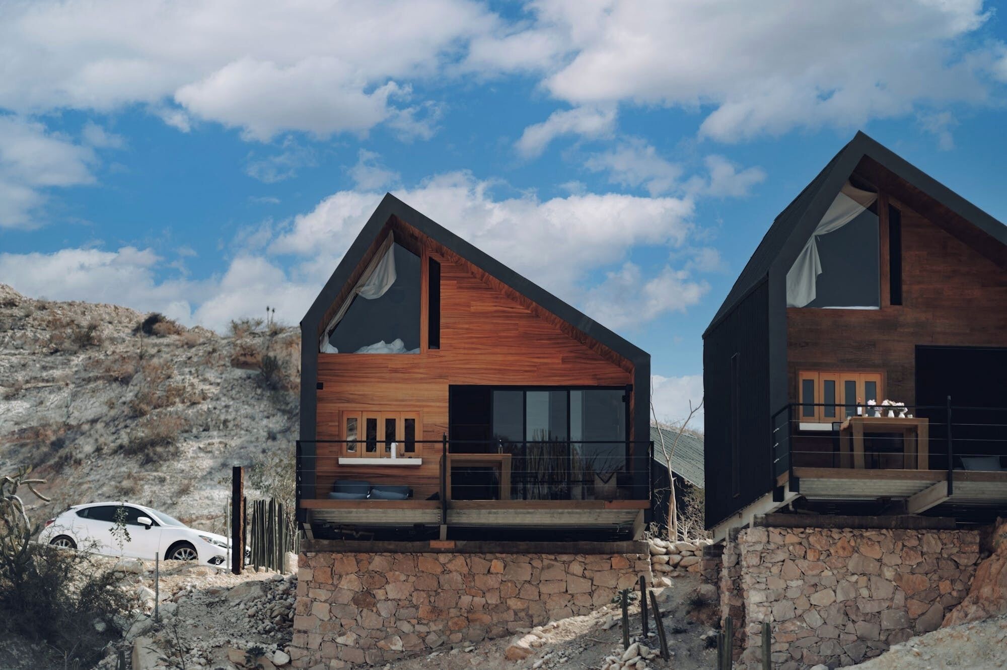 A modern two-story house with a stone foundation, large windows, and a wooden exterior.