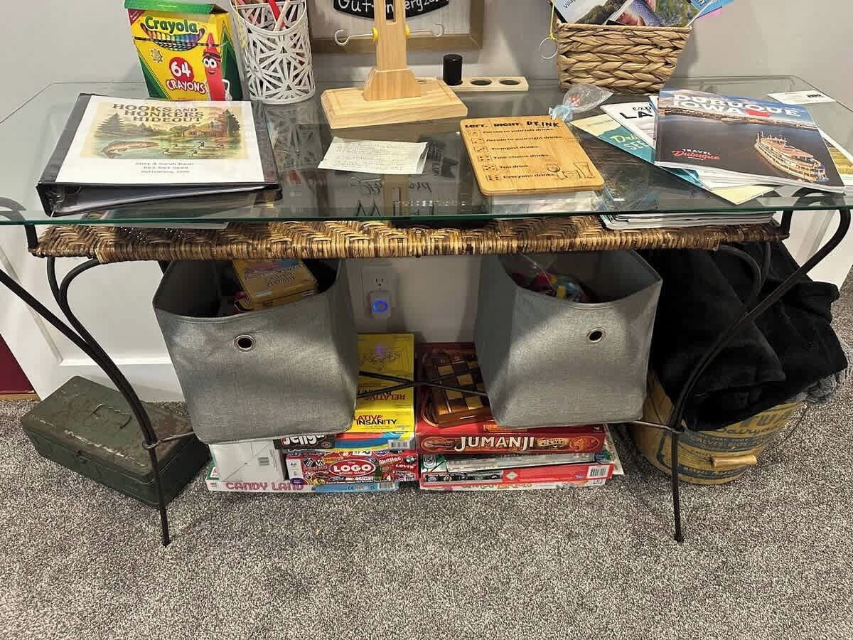 Una mesa con superficie de vidrio y base tejida, rodeada de cajas de almacenamiento y una cesta.