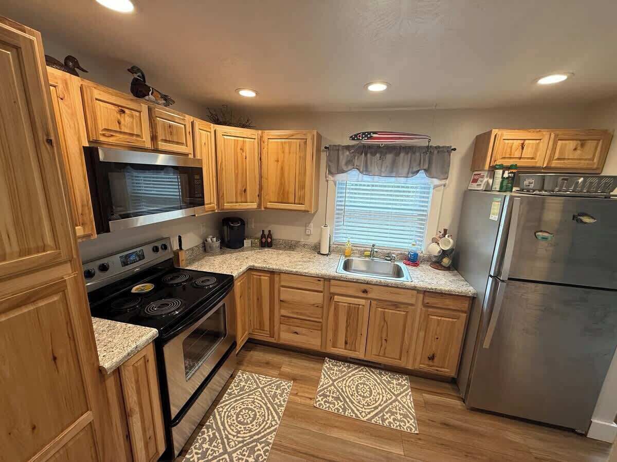 Cocina compacta con armarios de madera, refrigerador de acero inoxidable, estufa y ventana con persianas.