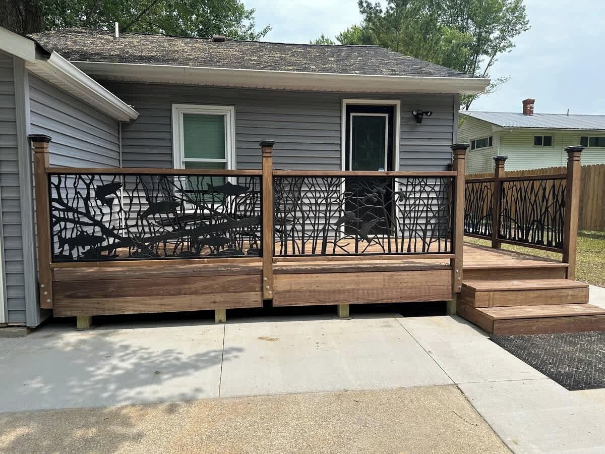 A residential deck with a wooden railing and a metal gate, leading to a house with a gray exterior and a green door.