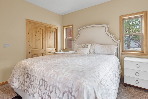 A bedroom with a large bed, a wooden wardrobe, a window with a view of trees, and a white dresser. - Boulder Bay Chalet Lakefront (Big Bear Lake)