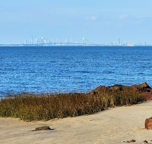 A coastal view with a sandy beach, rocky outcrops, and a city skyline in the distance.
